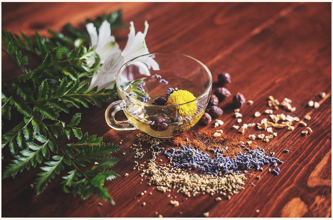 Clear glass cup of herbal tea with dried flowers and spices on a wooden surface