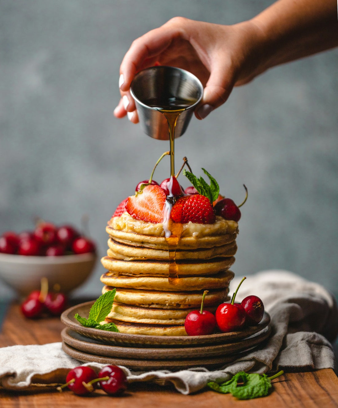 Dark syrup being poured over a stack of pancakes