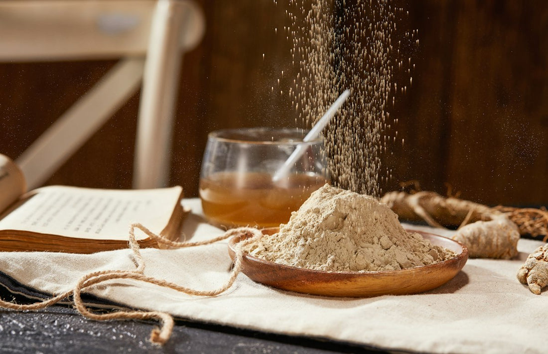 Tan root powder piled in a wooden dish beside dried roots