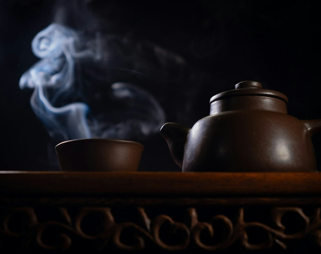 Steaming ceramic teapot and cup on a dark table