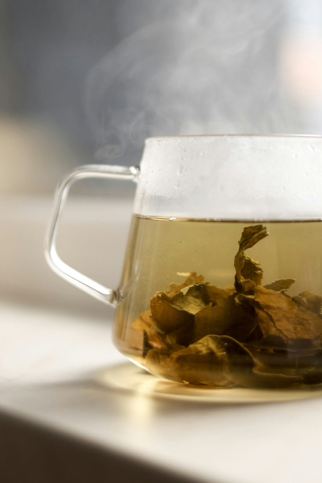Steaming glass mug of herbal tea with whole leaves steeping